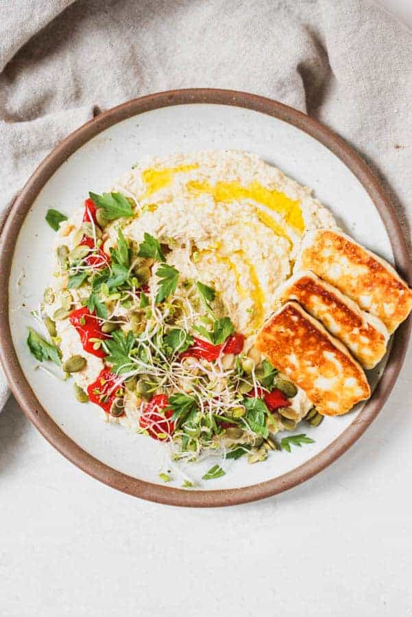 Hummus on a plate with toasted cheese and herbs.